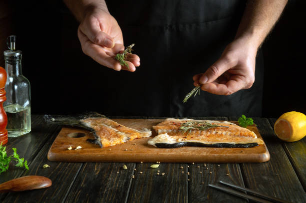 istock Chef preparing fresh red fish on the kitchen table in a restaurant. Before frying, fish steaks are seasoned with aromatic rosemary. European cuisine 1907140941