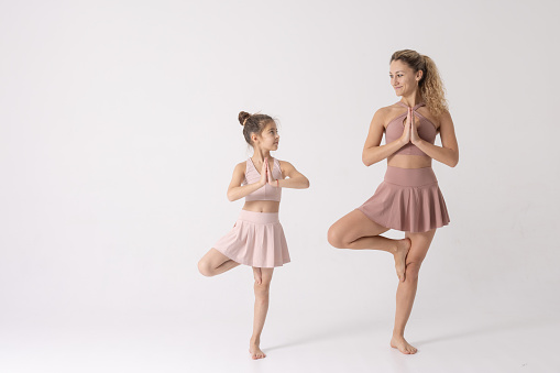 Mother and daughter doing exercise on a white background, two girls do fitness