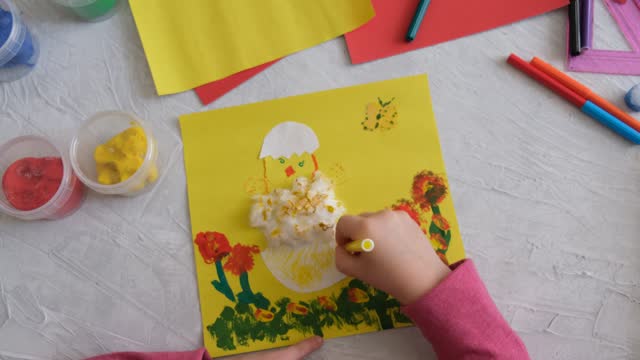 Child creating card with Easter funny eggs and flowers from colorful paper.