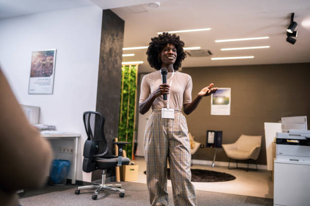 istock Young business woman lecturing her multiethnic colleagues. Having a speech while holding a microphone. 1907186886