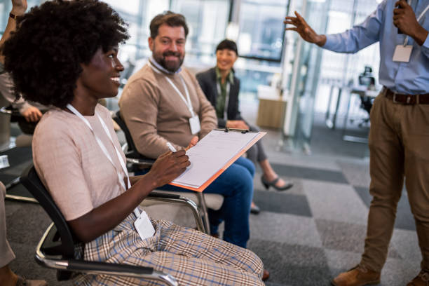 istock Young bussines man lecturing his multiethnic colleagues. Having a speach while holding a microphone. 1907191300