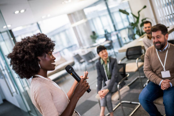 istock Young business woman lecturing her multiethnic colleagues. Having a speech while holding a microphone. 1907191302