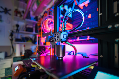 3D printer with a printed object on the table. The interior of a home workshop. Wall with tools in the background. Colorful backlight