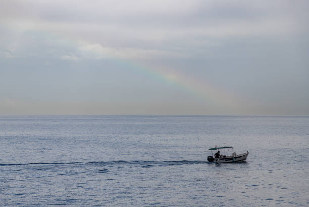 Chania, Crete, Greece - September 27, 2023: A picture of a fishing boat on the sea with a rainbow in the distance.