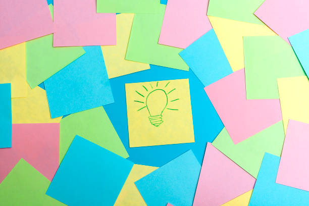 istock Yellow notepaper with a painted burning lamp lies on a blue background between colored pieces of paper The concept of a found idea is an epiphany. 1907271288