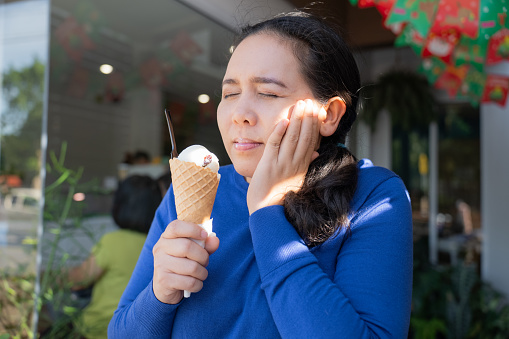 Asian woman feeling sensitive teeth after eating ice cream causing from suffer tooth and decay problems requiring dental care.
