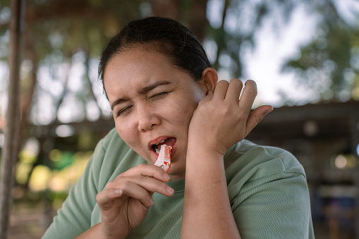 Close up shot of Asian woman using her teeth to cut and grind the rigid food and feeling suffered because of her toothache illness.