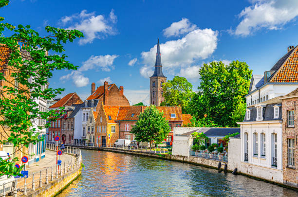 Sint Annarei water canal of Reie river, old buildings on embankment in Brugge old town, Bruges city historical centre, Saint Anna Church tower spire, West Flanders province, Flemish Region, Belgium canal de agua de sint annarei del río reie, edificios antiguos en el terraplén en el casco antiguo de brujas, centro histórico de la ciudad de brujas, torre de la torre de la iglesia de santa ana, provincia de flandes occidental, región flamenca, bélg