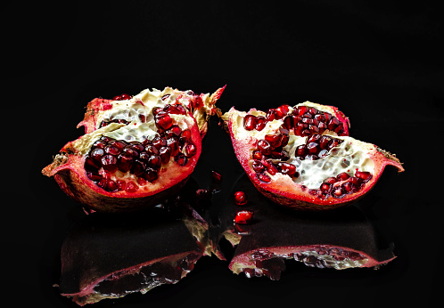 Sliced whole red pomegranate on shiny background. Reflections of pomegranate fruits