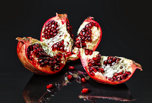 Sliced whole red pomegranate on shiny background. Reflections of pomegranate fruits