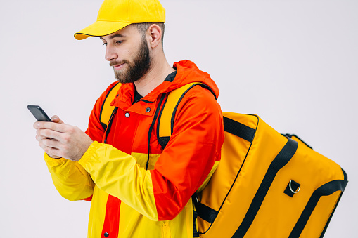 Courier with a backpack and a smartphone in his hands. A courier in a yellow jacket checking social media while waiting for an order.