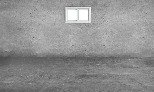Empty dark basement room with a cement flooring and a concrete wall with a small window