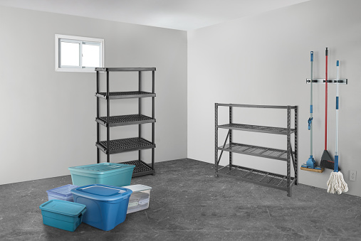 A basement room with storage racks, totes and cleaning mops and brooms