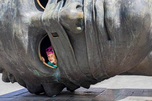 Krakow, Poland - July 18, 2023: Little child looking through eye of Eros Bendato giant head statue at Rynek GlownyKrakow Malopolska region in Poland