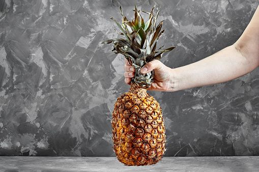 Pineapple in hands on cement background. Food delivery