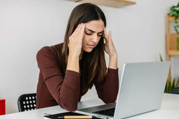 istock Young business woman having headache working on laptop computer at home office 1907358371