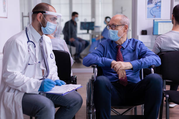 istock Paralized elderly man with face mask sitting in wheelchair talking with doctor 1907364092