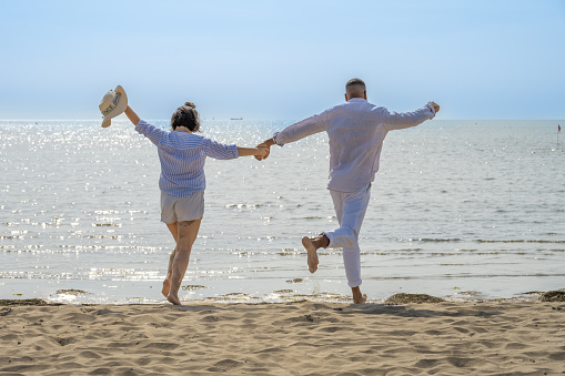 Couple with holding hands while running on beach during vacation in sunny day.