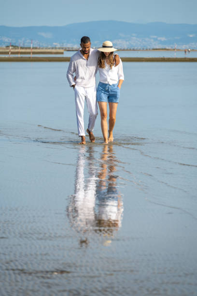 couple walking on beach - women wading sun hat summer 뉴스 사진 이미지