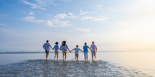 Rear view of multi generation family walking on beach against sky during vacation in sunny day.