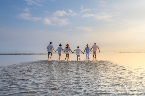 Rear view of multi generation family walking on beach against sky during vacation in sunny day.