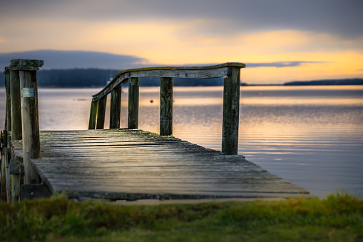 A wooden dock extends out into the tranquil lake at sunset