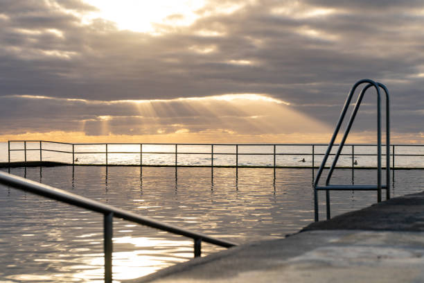 istock Metal railing by a tranquil sea illuminated by a warm golden sunset 1907381783