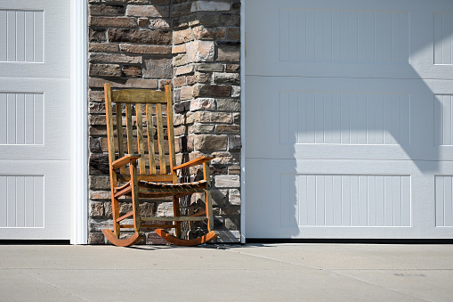 Wooden rocking chair on the driveway by the garage doors.