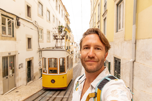He takes a selfie with the yellow cable car in a famous street.\nPeople enjoying their neighbor country traveling in Europe for a weekend.\nStaycation concept