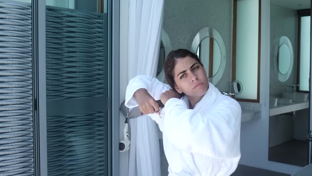 Beautiful woman in bathrobe looking out the window in the bathroom
