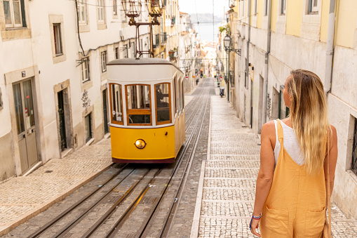 She walks by the yellow cable car in a famous street.\nPeople enjoying their neighbor country traveling in Europe for a weekend.\nStaycation concept