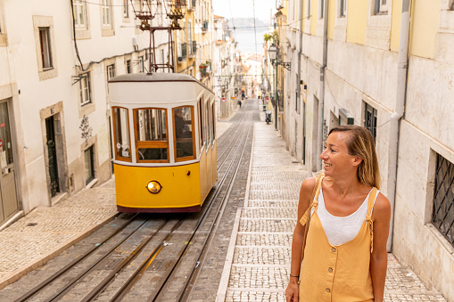 She walks by the yellow cable car in a famous street.\nPeople enjoying their neighbor country traveling in Europe for a weekend.\nStaycation concept