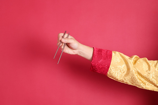 Happy Chinese new year. Asian Chinese energetic senior man wearing golden traditional cheongsam qipao or changshan dress with gesture of hand holding silver chopsticks isolated on red background.