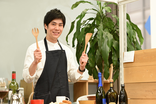 A young Asian male waiter at a restaurant is smiling and looking at the camera while holding cutlery.