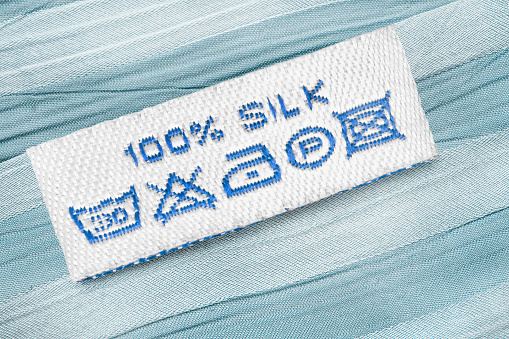 Fabric composition and washing instructions clothes label on blue silk closeup