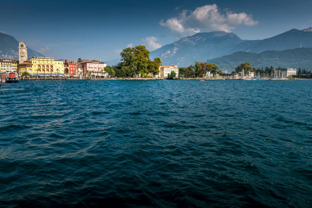 Riva del Garda, Italy - October, 04. 2023: View from waterside to town square downtown Riva del Garda with restaurants and clock tower near harbor.