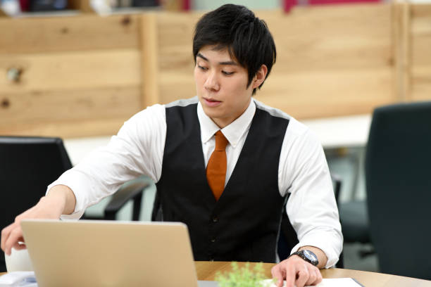 istock Asian young male office worker working on laptop while having a drink indoors 1907526702