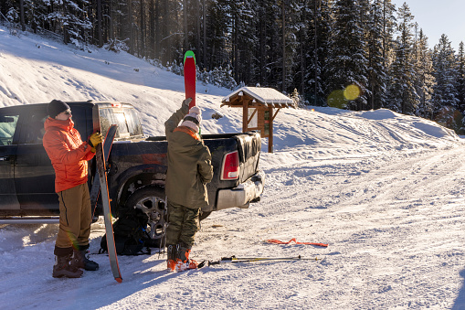 Friends prepare to backcountry ski together and remove skis from truck
