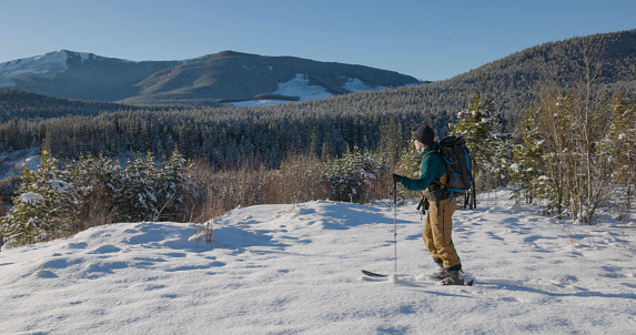 Young man backcountry skis in clearing on a sunny winter day
