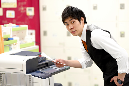 Asian young male office worker checking documents in front of the office printer