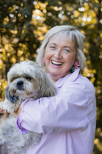 ortrait of happy smiling mature woman with her pet terrier in her arms in the garden