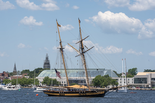 Annapolis, Maryland, United States - 4 June 2022: A large yellow sailboat on the Severn River with the United States Naval Academy in the background.