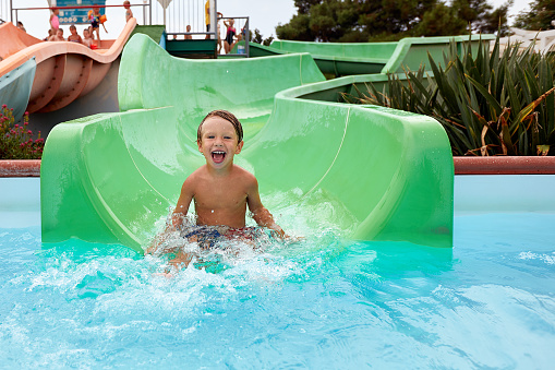 Joyful boy descends from the water slide in the water park, children's attractions in the water park, water slides, children's entertainment on vacation.
