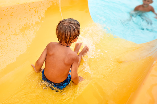 Joyful boy descends from the water slide in the water park, children's attractions in the water park, water slides, children's entertainment on vacation.