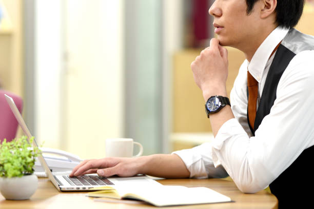 istock Young Asian male office worker thinking while working on laptop in office 1907616357