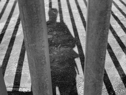 Shadow of man and vertical bars of fence in the street