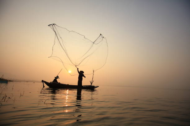 istock Silhouette fisherman on boat throwing net in lake 1907627974
