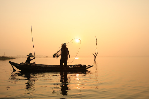 Lifestyle of Asian fisherman on wooden boat for catching freshwater fish in reservoir in the early morning before sunrise