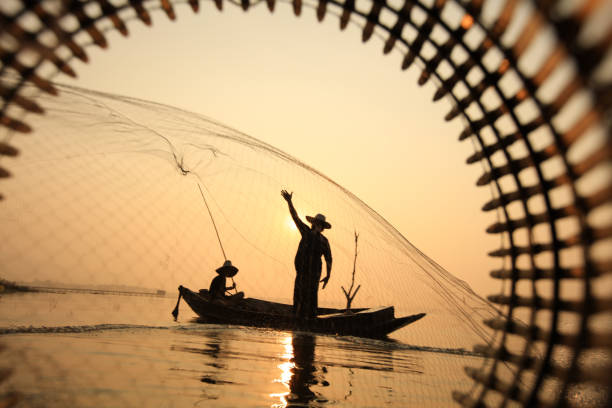 istock Silhouette fisherman on boat throwing net in lake 1907628497