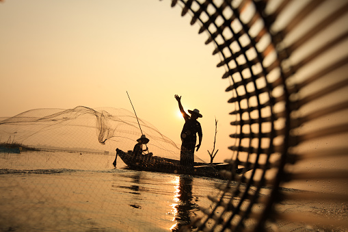 The silhouette fisherman on a boat fishing by throwing a fishing net